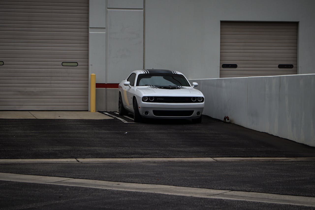 A white Dodge Challenger sports car parked in an urban industrial area with rolled-up garage doors.